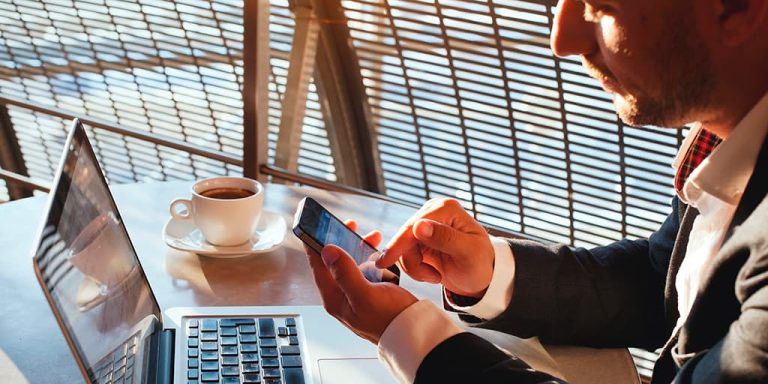 Persona trabajando con ordenador portátil y teléfono móvil en una cafetería