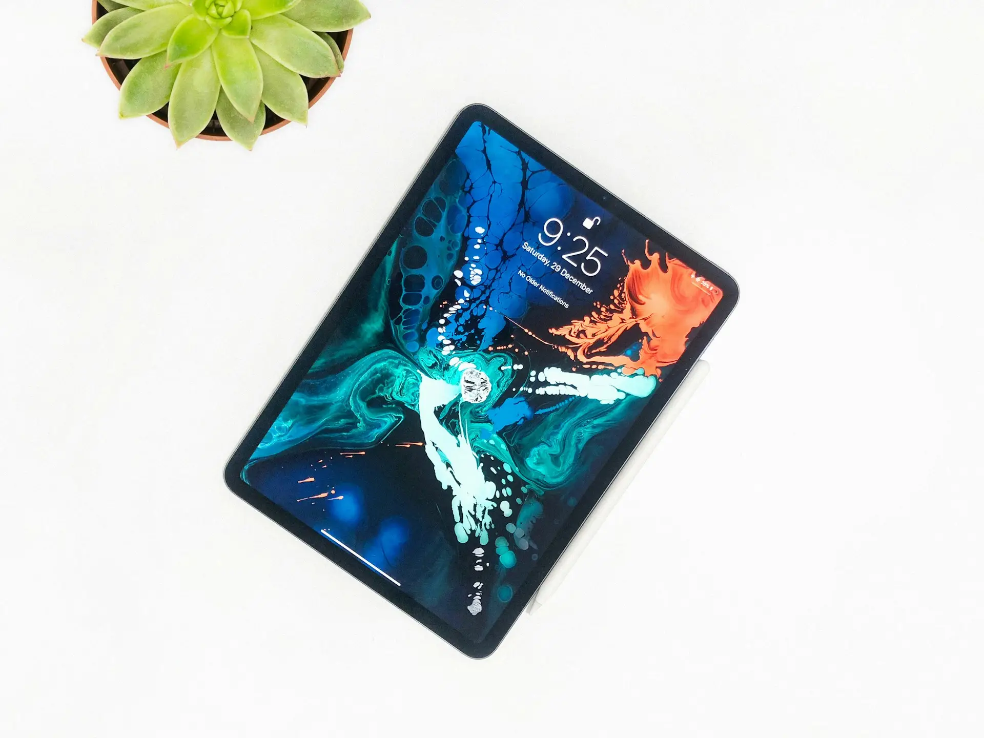 Tablet iPad Pro con pantalla encendida mostrando un fondo abstracto de colores azul y verde junto a un lápiz digital Apple Pencil sobre fondo blanco.